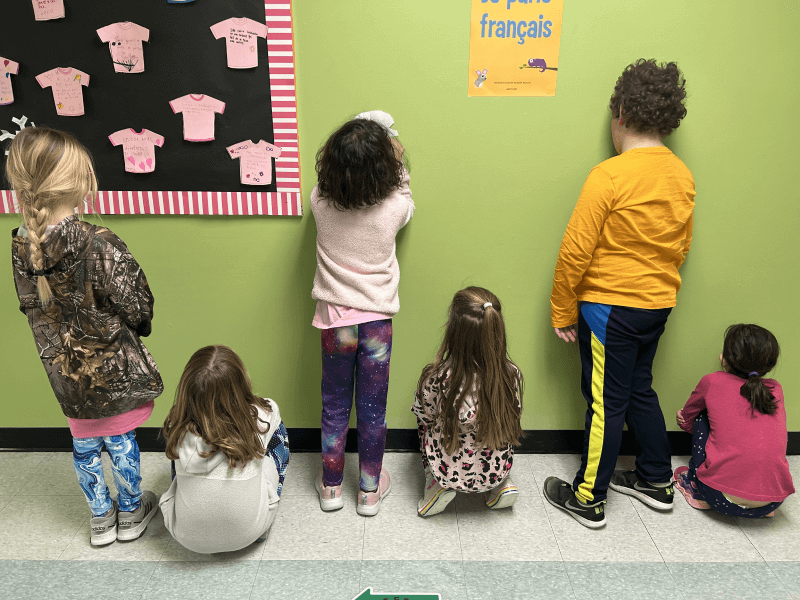 Des enfants dans une salle de classe. Leurs corps forment une série, de droite à gauche : l' enfant 1 est accroupi, l'enfant 2 est debout, l'enfant 3 est accroupi, l'enfant 4 est debout, l'enfant 5 est accroupi, l'enfant 6 est debout.