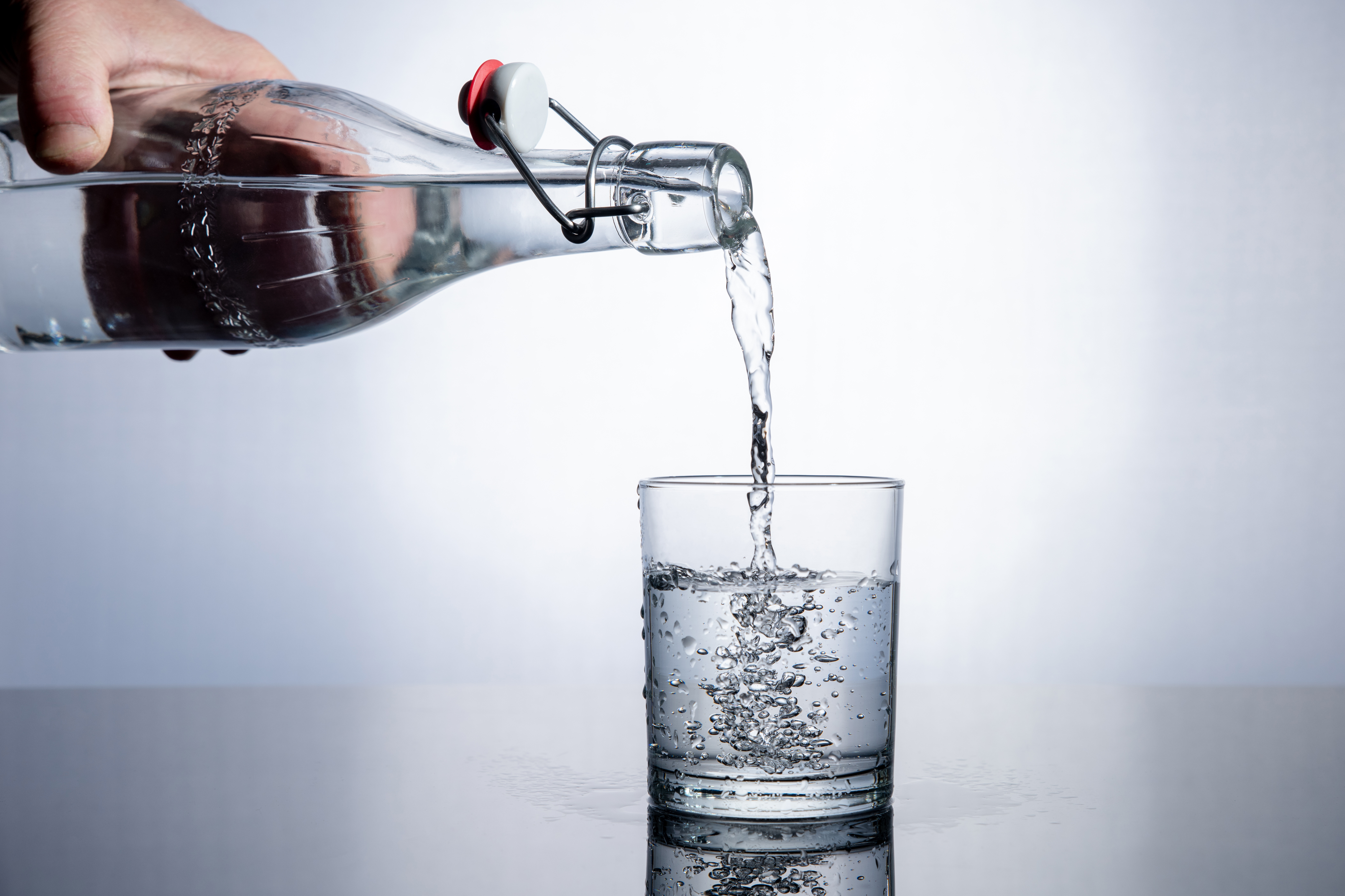 Une main tient une bouteille d’eau et verse de l’eau dans un verre.