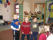 Situation de salle de classe.  Il y a trois élèves debout dans un cerceau. Il a d’autres élèves dans la classe.