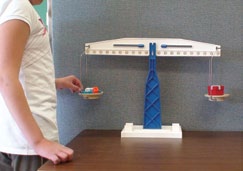 A student measures the mass of two objects with a tray scale.