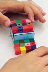 A student works with paper prisms and interlocking cube prisms.