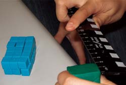 A student measures one side of a modeling clay prism.