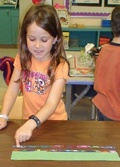 Une élève utilise des trombones de petite et grande teille pour mesurer un carton.